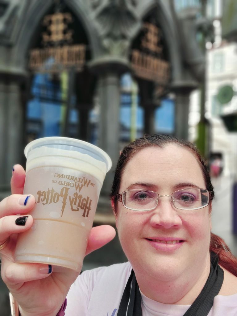 "A travel agent confidently and proudly hold up an ice-cold Butterbeer at The Wizarding World of Harry Potter--an affordable indulgence that brings magic to life without breaking the bank."